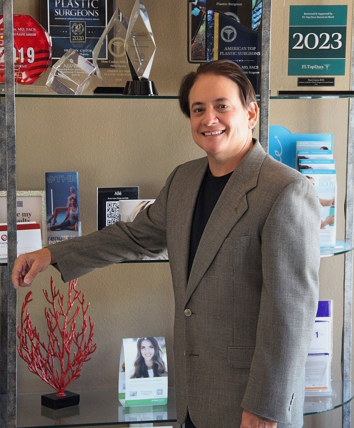 Plastic surgeon in office with awards displayed.