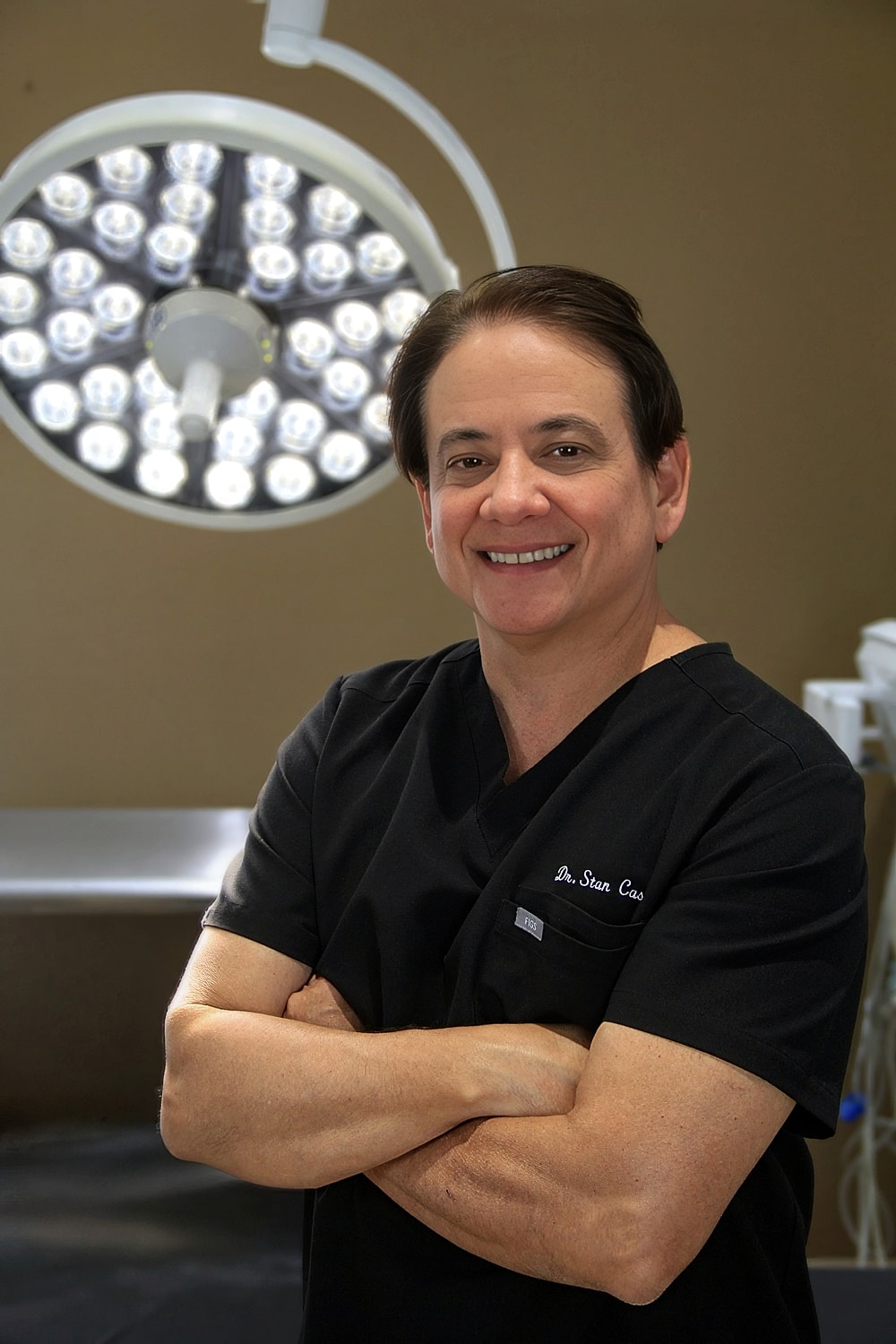 Smiling doctor in surgical scrubs, operating room background.