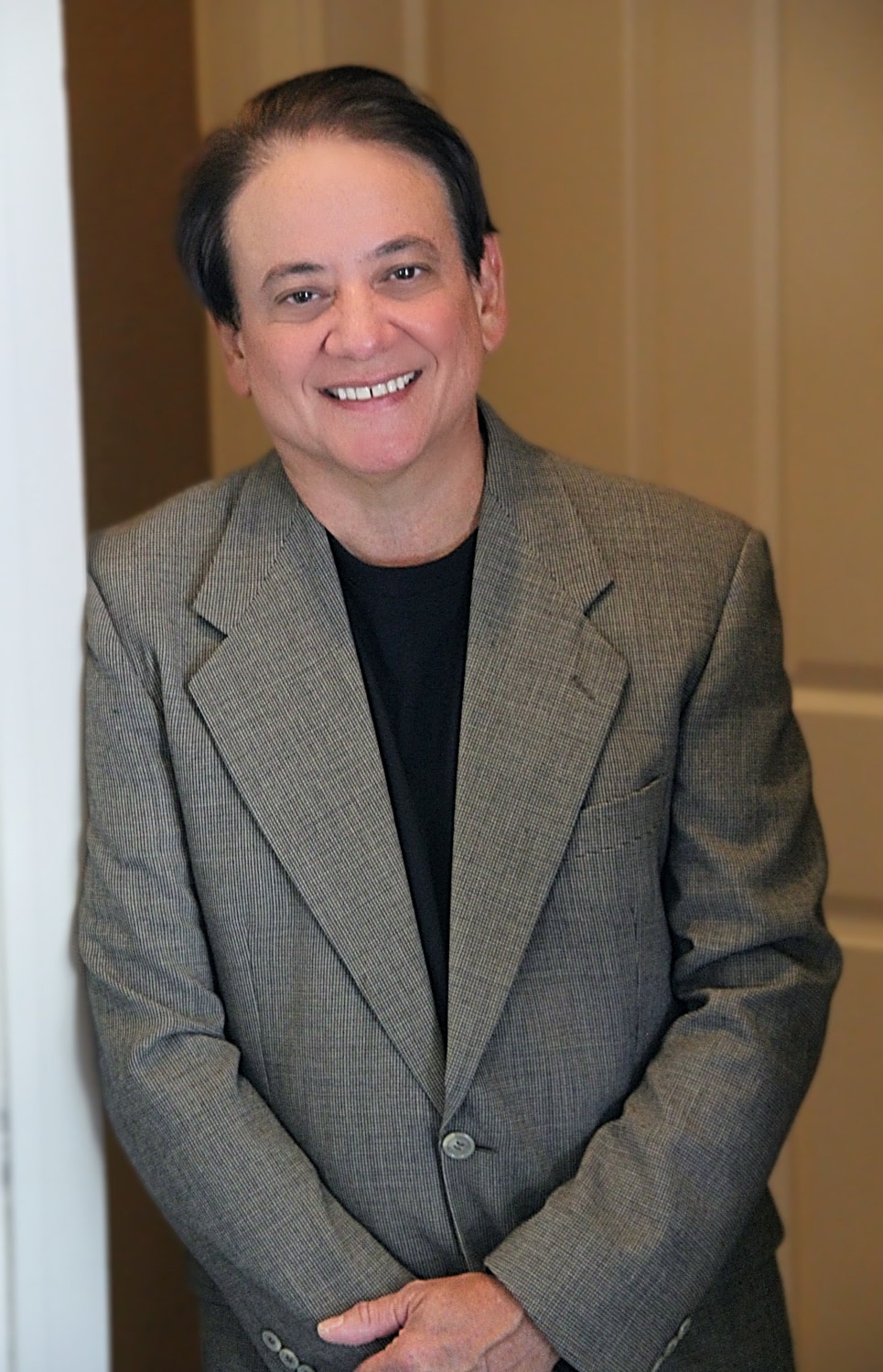 Smiling man in a blazer, standing indoors.