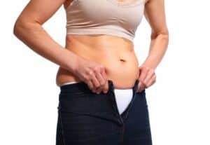 Woman trying to close her pants over her stomach without her compression garment for tummy tuck recovery